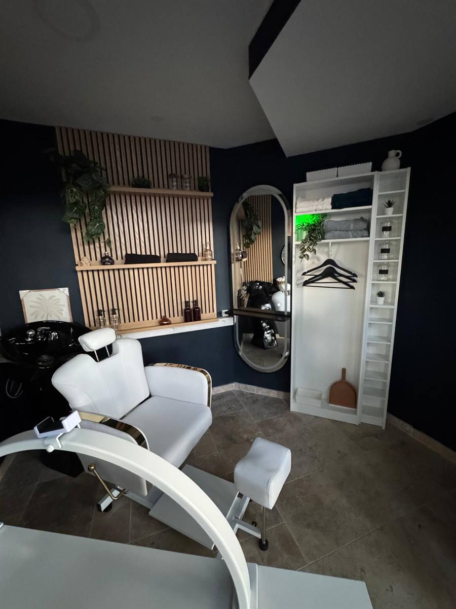 Le coin coiffure de l'espace beauté de la Laverie Jaurès : bac à shampoing noir laqué, fauteuil blanc et or, mur en tasseaux de bois clair et grand miroir ovale doré.